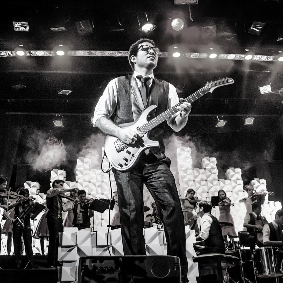Guitar solo with the Camerata (by Antonio Dávila) Everton Vidal Azevedo leading a guitar performance with the Camerata del Oriente ensemble behind him, black-and-white image. Una Canción Hecha Mujer. Photo by Antonio Dávila.