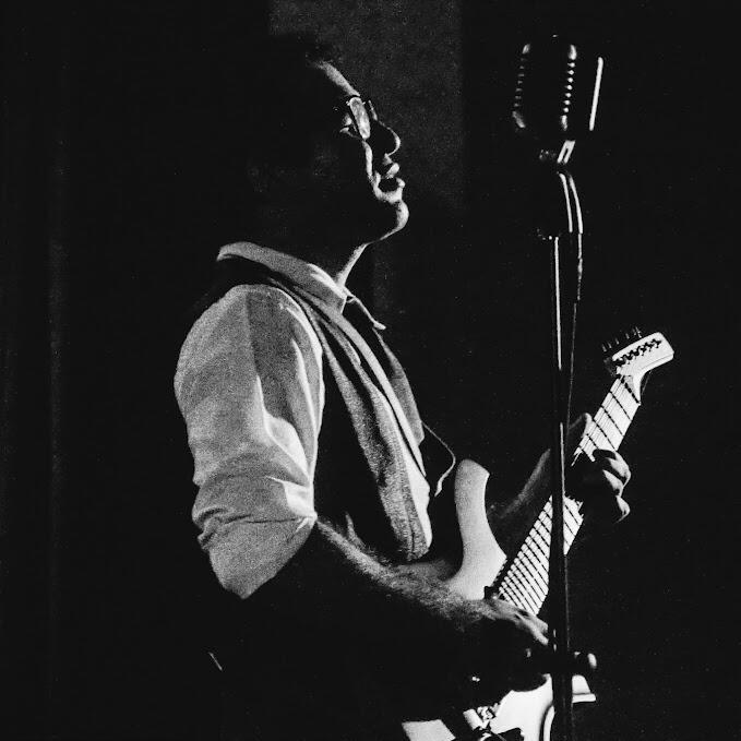 In the spotlight (by Antonio Dávila). Side view of Everton Vidal Azevedo singing and playing guitar during a Camerata del Oriente concert - Una Canción Hecha Mujer- black-and-white photography (by Antonio Dávila).