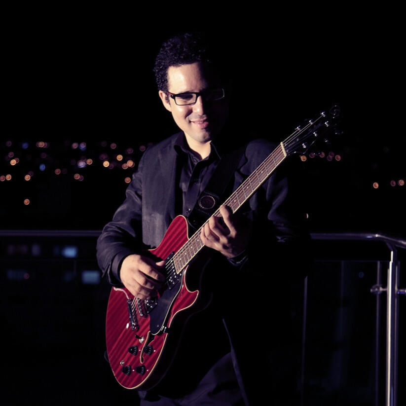 Night session above Scz (by Claudio Arduz) Everton Vidal Azevedo performing with a red semiacoustic guitar on a rooftop (Hotel Cortez) in Santa Cruz de la Sierra, photo by Claudio Arduz.