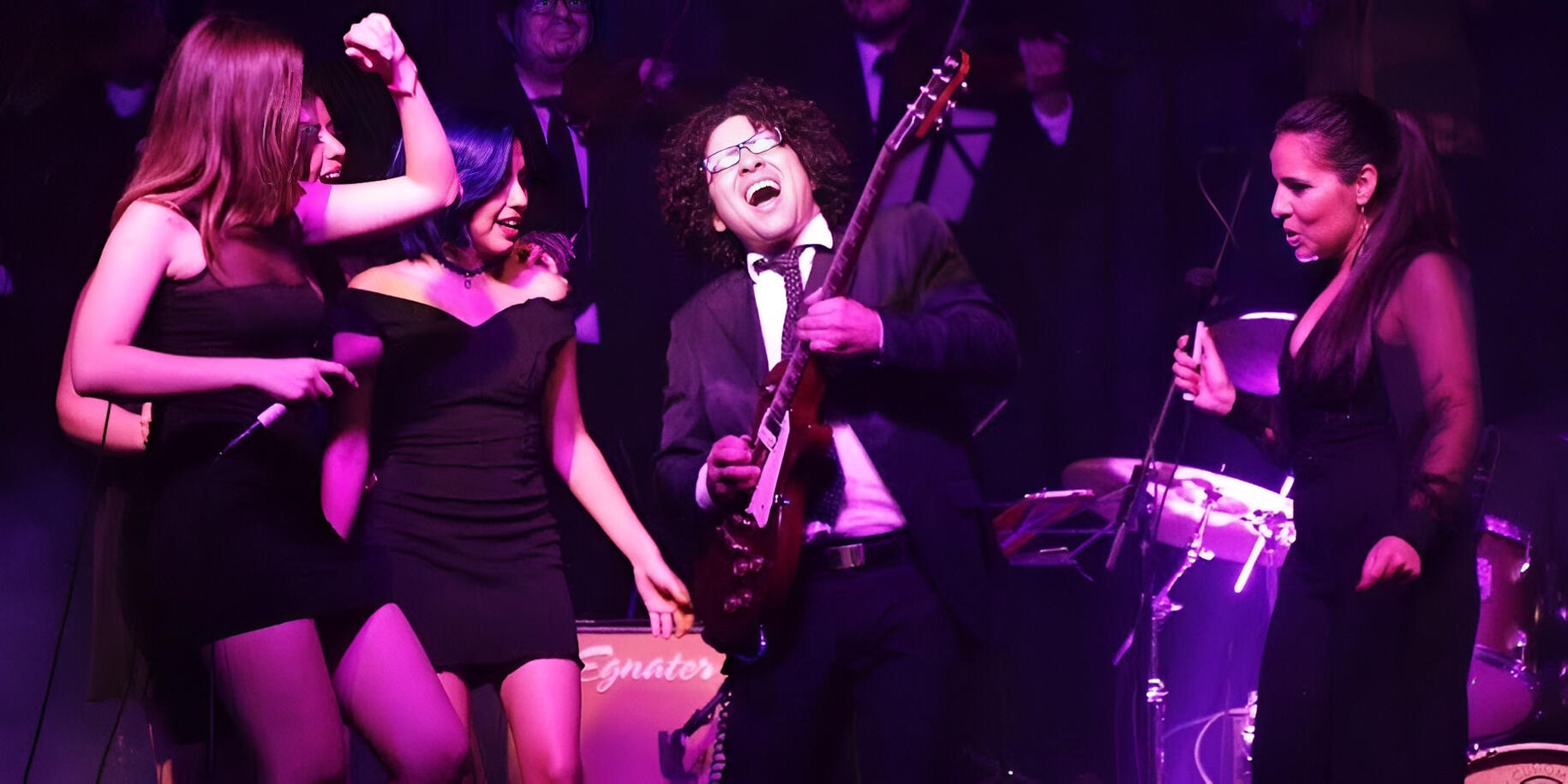 Girl Power with the Camerata — performing with Jessi Luna, Yna & Lizzett Everton Vidal performing live with the Camerata del Oriente during the Girl Power concert, sharing the stage with vocalists Jessi Luna, Yna, and Lizzett under vibrant pink and purple lights.